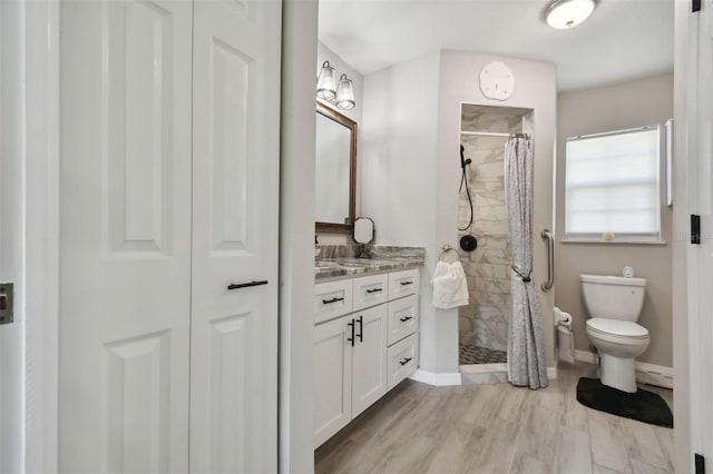 full bath with vanity, wood finished floors, baseboards, tiled shower, and toilet