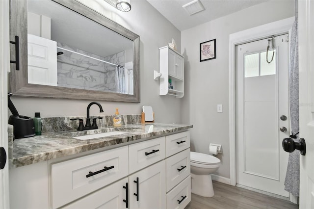 bathroom featuring vanity, a shower with shower curtain, wood finished floors, visible vents, and toilet