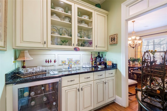 bar with cream cabinetry, decorative light fixtures, dark stone countertops, and beverage cooler