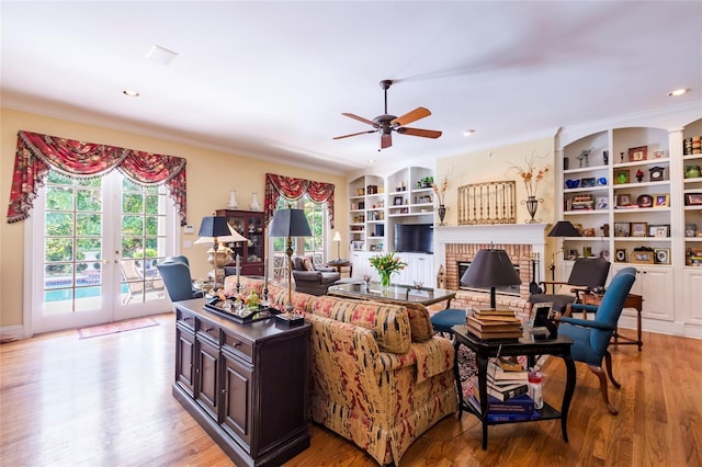 living room featuring french doors, built in shelves, ceiling fan, a fireplace, and light hardwood / wood-style floors