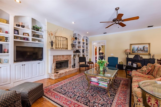 living room with ornamental molding, built in shelves, ceiling fan, hardwood / wood-style flooring, and a fireplace