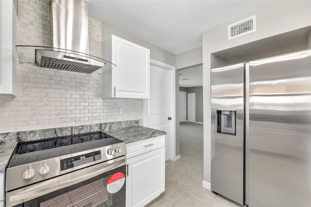 kitchen with stainless steel appliances, white cabinetry, dark stone countertops, and wall chimney range hood