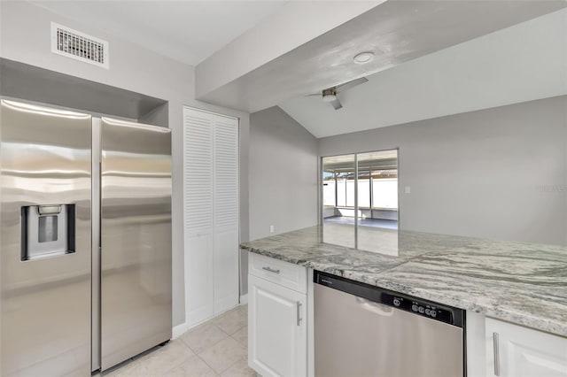 kitchen with light stone countertops, stainless steel appliances, vaulted ceiling, white cabinets, and light tile patterned flooring