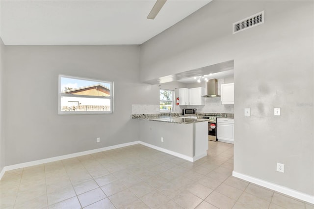 kitchen with lofted ceiling, kitchen peninsula, wall chimney exhaust hood, white cabinetry, and stainless steel appliances