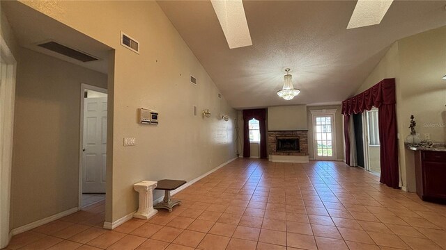 unfurnished living room with a stone fireplace, light tile patterned floors, a textured ceiling, and high vaulted ceiling