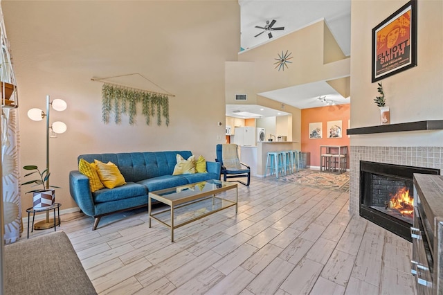 living room with ceiling fan, light hardwood / wood-style floors, a fireplace, and high vaulted ceiling