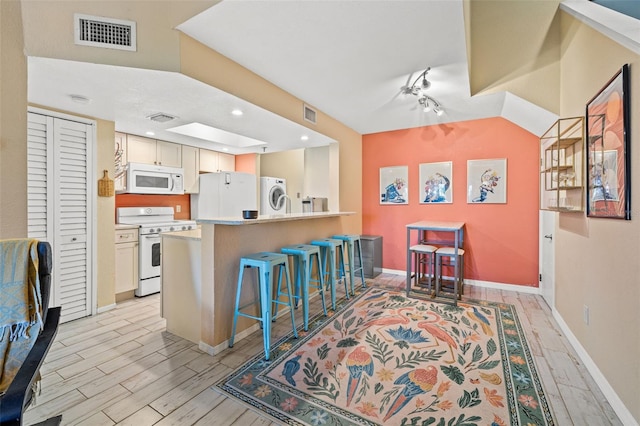 kitchen with a kitchen breakfast bar, light hardwood / wood-style floors, white appliances, and washer / clothes dryer