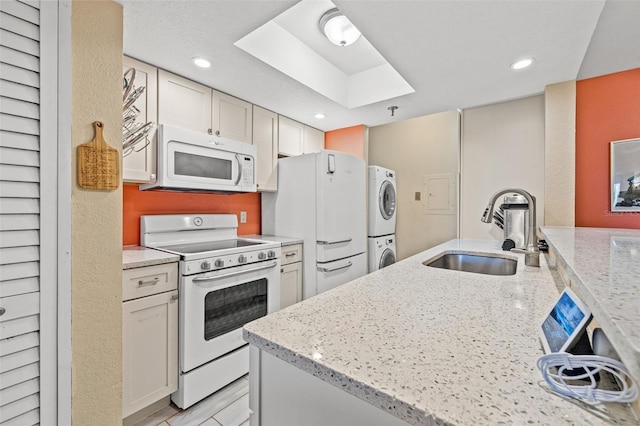 kitchen with white appliances, sink, light stone countertops, stacked washer / drying machine, and white cabinetry