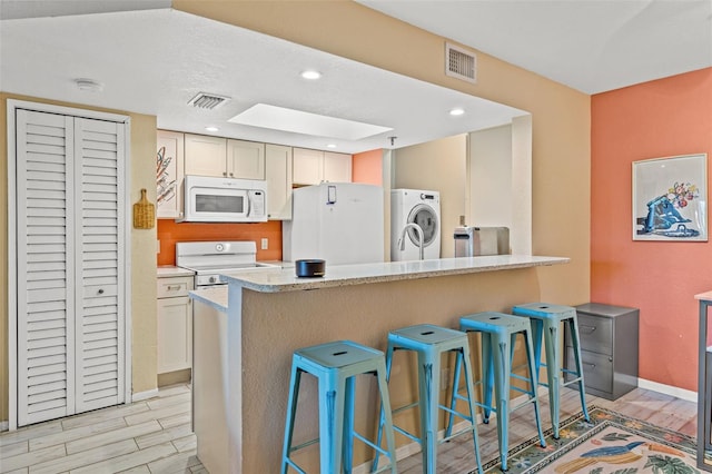 kitchen with light stone countertops, a breakfast bar, white appliances, washer / dryer, and light hardwood / wood-style floors