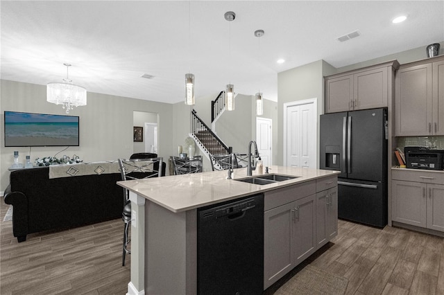 kitchen with a kitchen bar, sink, black appliances, hanging light fixtures, and an island with sink