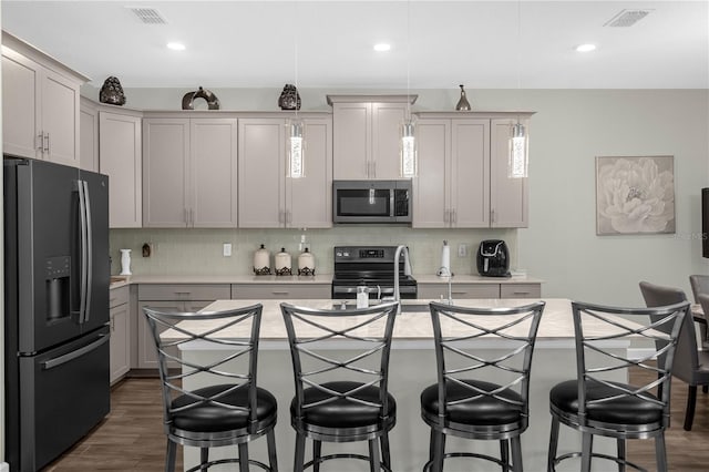 kitchen with a breakfast bar, an island with sink, appliances with stainless steel finishes, and dark wood-type flooring