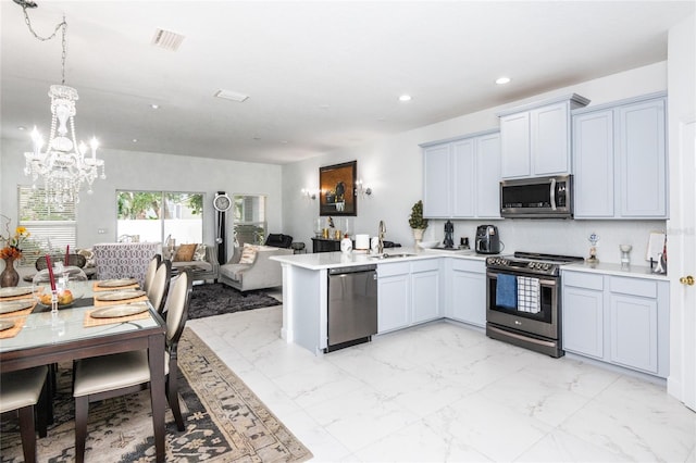 kitchen with kitchen peninsula, appliances with stainless steel finishes, sink, an inviting chandelier, and hanging light fixtures