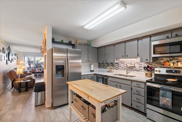 kitchen with gray cabinetry, light wood-type flooring, a textured ceiling, tasteful backsplash, and stainless steel appliances