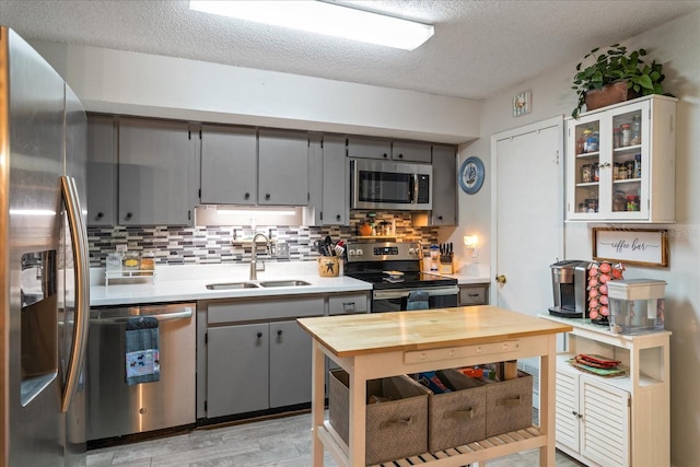 kitchen with a textured ceiling, stainless steel appliances, sink, light hardwood / wood-style flooring, and gray cabinets