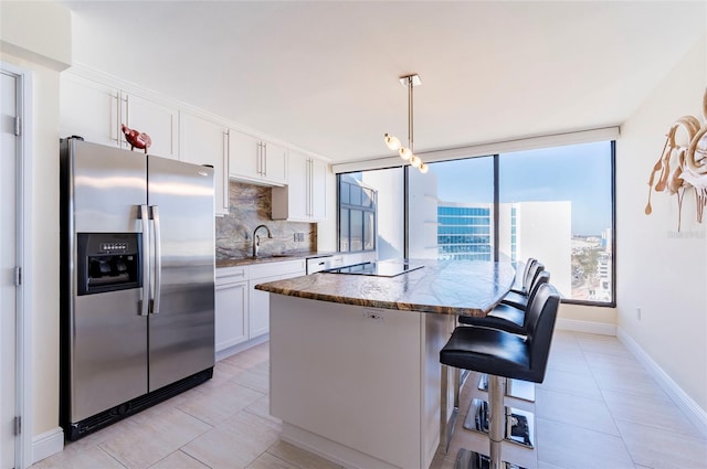 kitchen with pendant lighting, backsplash, white cabinets, stainless steel fridge, and an island with sink