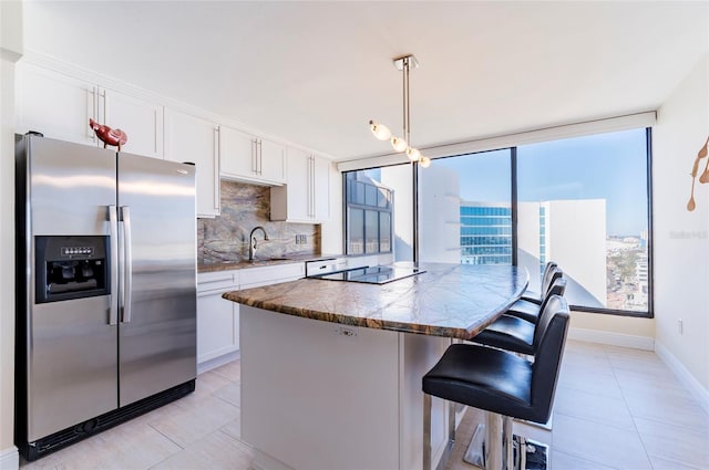 kitchen with white cabinetry, decorative backsplash, stainless steel fridge, and hanging light fixtures