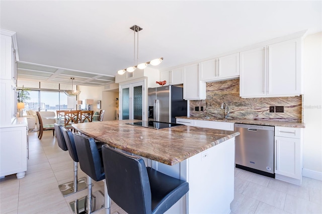 kitchen featuring stone counters, white cabinetry, a center island, decorative light fixtures, and appliances with stainless steel finishes
