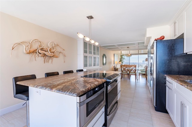 kitchen featuring a breakfast bar, stainless steel appliances, pendant lighting, dark stone countertops, and white cabinets