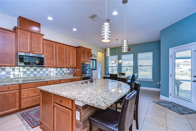 kitchen with pendant lighting, a breakfast bar, a kitchen island with sink, appliances with stainless steel finishes, and tasteful backsplash