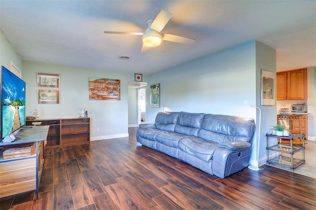 living room with a textured ceiling, ceiling fan, and dark wood-type flooring