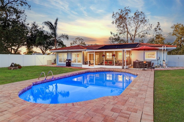 pool at dusk with a patio area, a yard, and grilling area