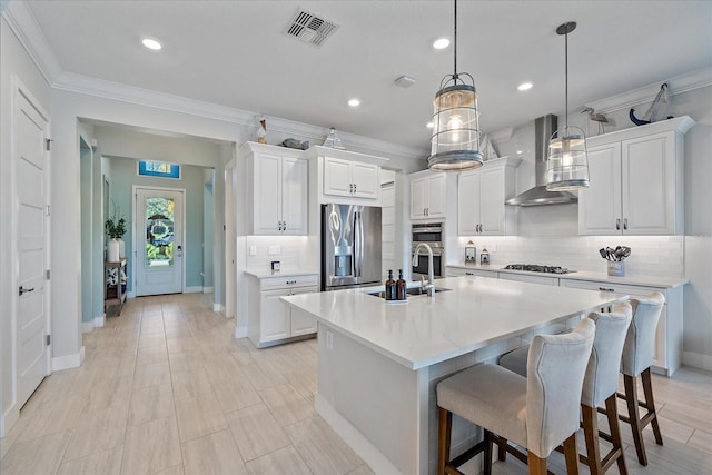 kitchen with white cabinetry, a kitchen island with sink, wall chimney exhaust hood, and stainless steel appliances