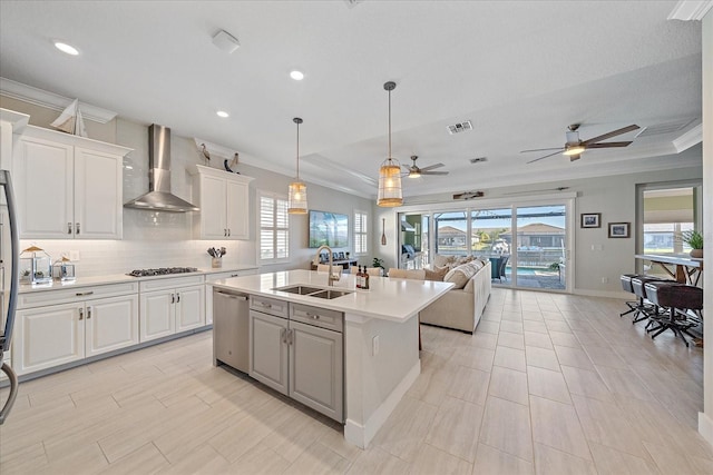 kitchen with a kitchen island with sink, white cabinets, sink, wall chimney exhaust hood, and appliances with stainless steel finishes