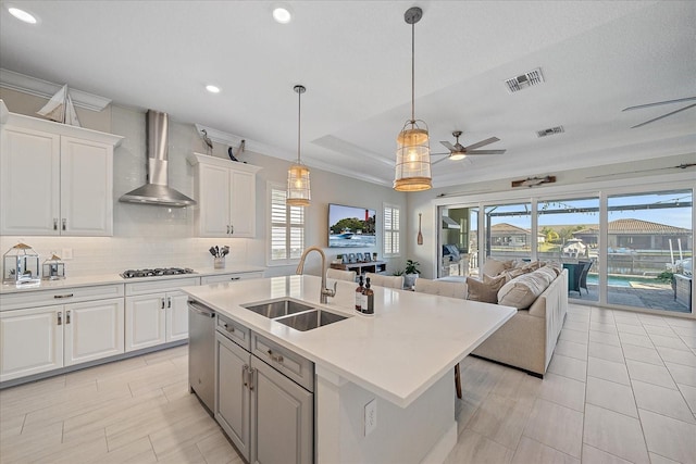 kitchen featuring ceiling fan, sink, wall chimney range hood, a center island with sink, and white cabinetry