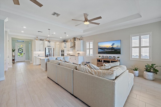 living room with a raised ceiling, crown molding, and ceiling fan