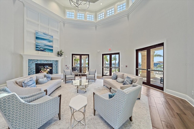 living room with light wood-type flooring, french doors, a towering ceiling, and a chandelier