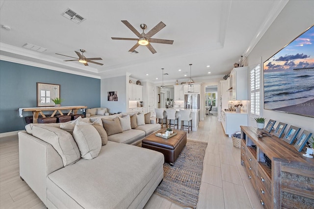 living room with plenty of natural light, a raised ceiling, visible vents, and crown molding