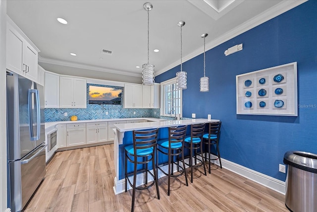 kitchen with a breakfast bar area, light wood-style flooring, light countertops, freestanding refrigerator, and crown molding