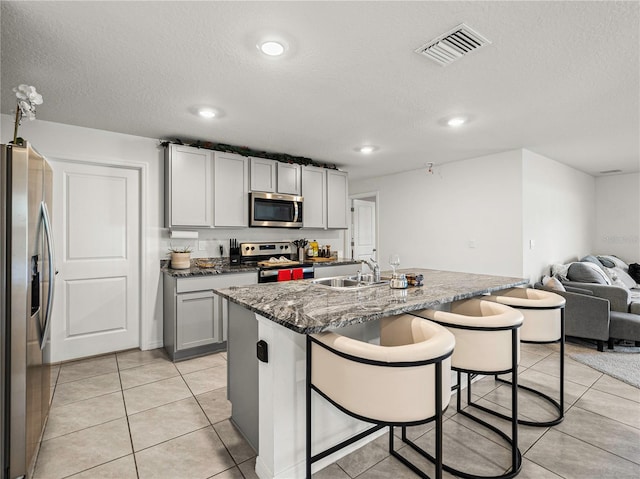 kitchen featuring dark stone counters, a textured ceiling, stainless steel appliances, sink, and a center island with sink