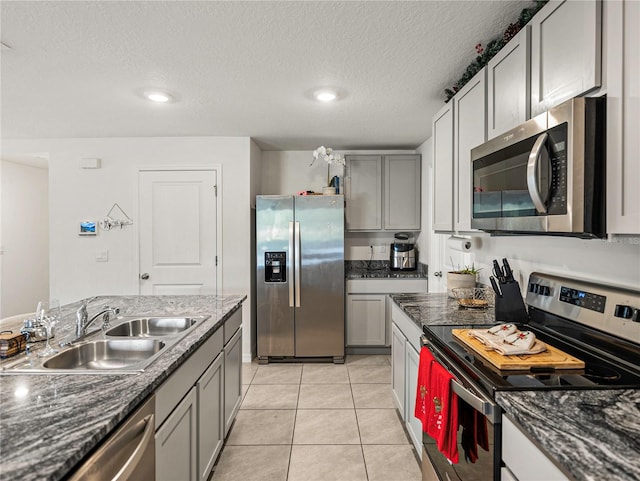 kitchen with gray cabinetry, sink, light tile patterned floors, a textured ceiling, and appliances with stainless steel finishes