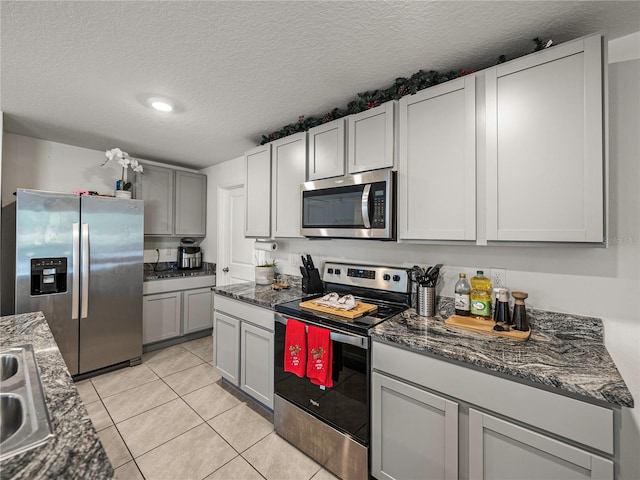 kitchen with sink, stainless steel appliances, dark stone countertops, a textured ceiling, and light tile patterned floors