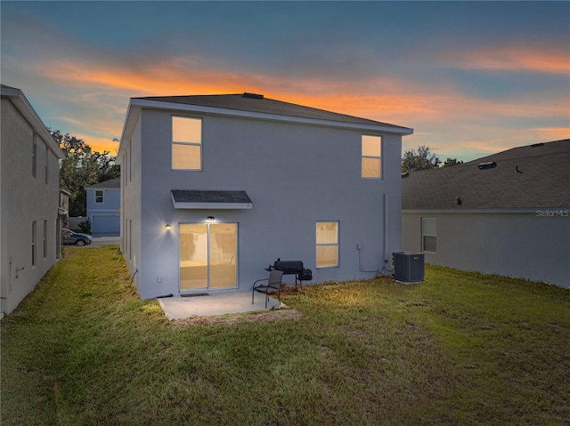 back house at dusk with a lawn, central air condition unit, and a patio