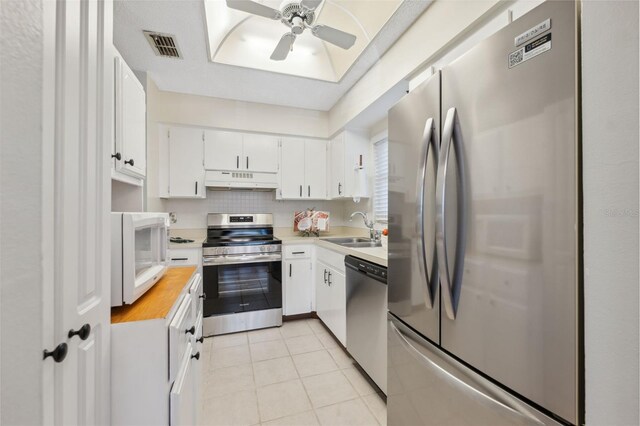 kitchen featuring sink, light tile patterned floors, ceiling fan, stainless steel appliances, and white cabinets