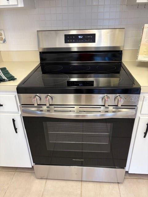 kitchen with electric stove, white cabinetry, decorative backsplash, and light tile patterned floors