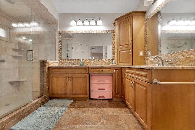 full bathroom featuring double vanity, tasteful backsplash, a sink, and a shower stall