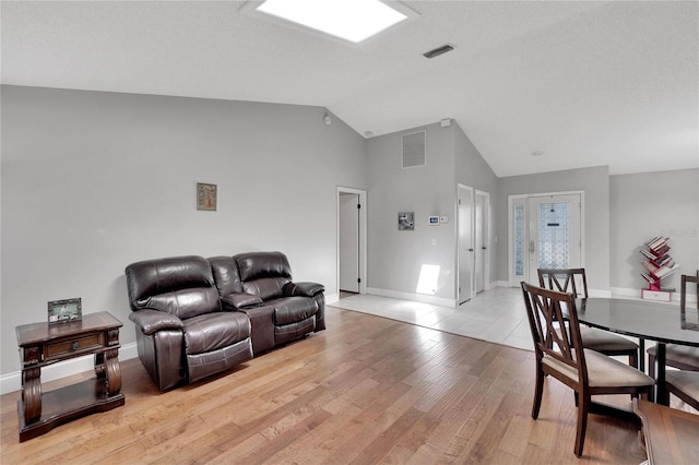 living area featuring lofted ceiling, light wood-style floors, baseboards, and visible vents