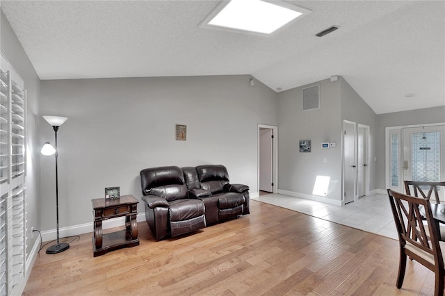 living room with lofted ceiling, a textured ceiling, light wood-style flooring, visible vents, and baseboards