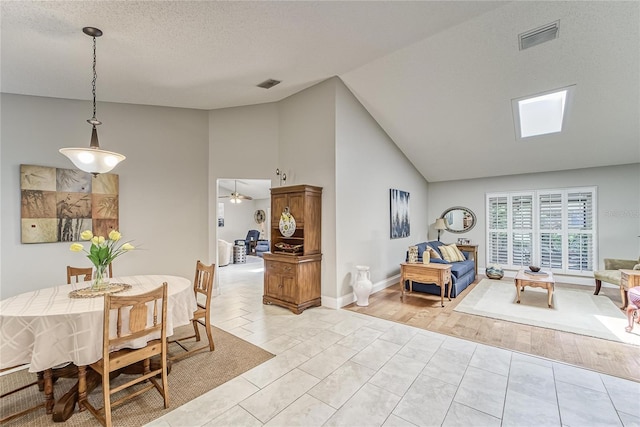 dining area with light wood finished floors, a textured ceiling, visible vents, and high vaulted ceiling