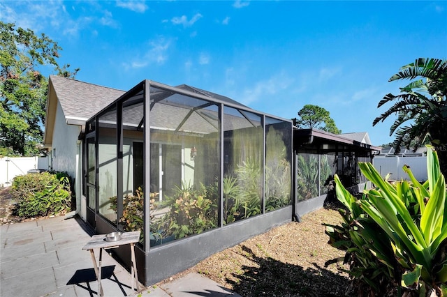 view of home's exterior featuring a lanai, a shingled roof, fence, and stucco siding