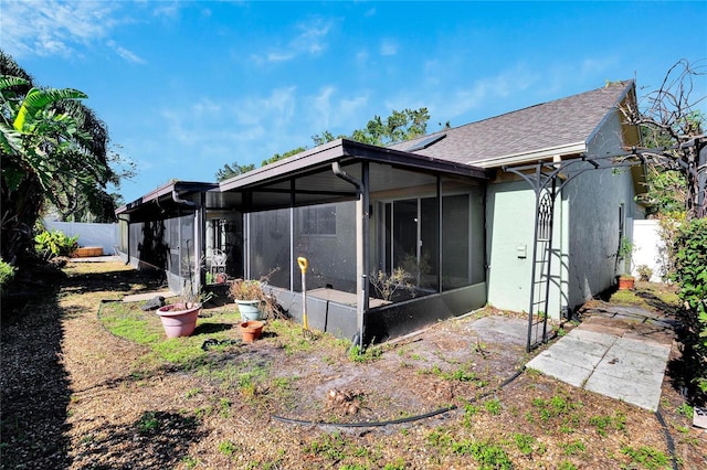 rear view of house featuring a shingled roof, fence, a sunroom, and stucco siding