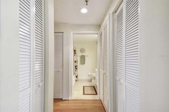 hall with a textured ceiling and light wood-type flooring