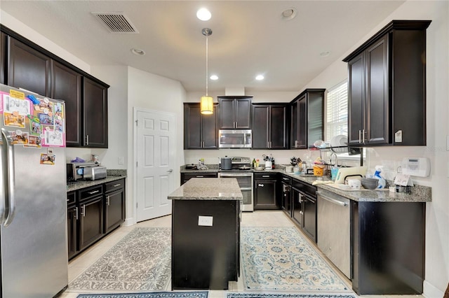 kitchen featuring appliances with stainless steel finishes, light stone counters, dark brown cabinetry, decorative light fixtures, and a kitchen island