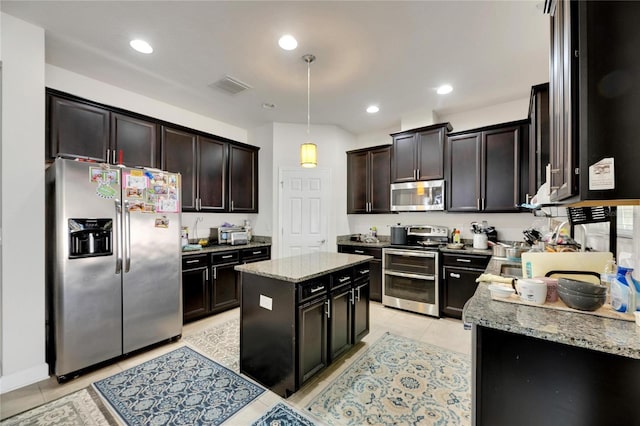 kitchen featuring light stone countertops, appliances with stainless steel finishes, dark brown cabinets, decorative light fixtures, and a kitchen island