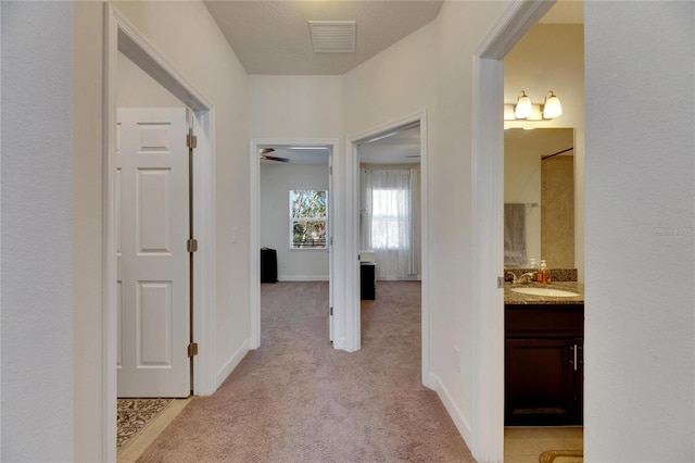 hall with light colored carpet and sink