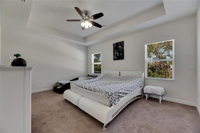 carpeted bedroom with ceiling fan and a raised ceiling