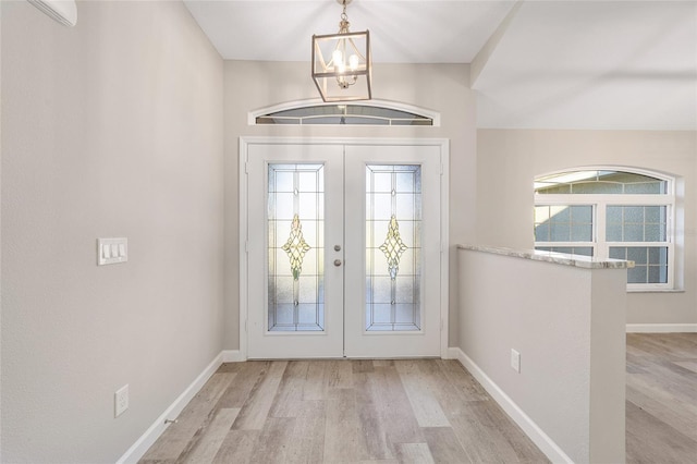 foyer entrance with a wall mounted air conditioner, a notable chandelier, light wood-type flooring, and french doors